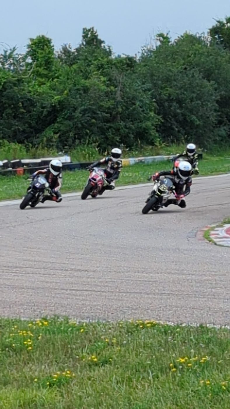 Three helmeted minimoto riders leaned over through a corner at Lombardy Raceway